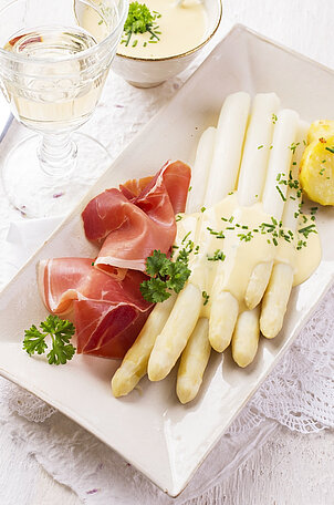 Leckerer, zubereiteter Spargel mit Sauce, Schinken, Petersilie und Kartoffeln